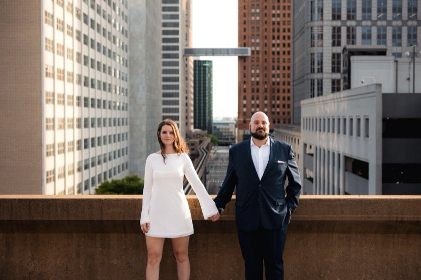 Sarah and Francesco on a rooftop, holding hands, with downtown Detroit behind them.